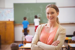 teacher in a classroom with students writing on a chalkboard in background