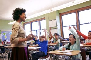 teacher standing in front of classroom of students with raised hands