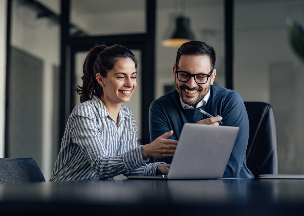 woman and man sitting in front of a laptop in an office setting