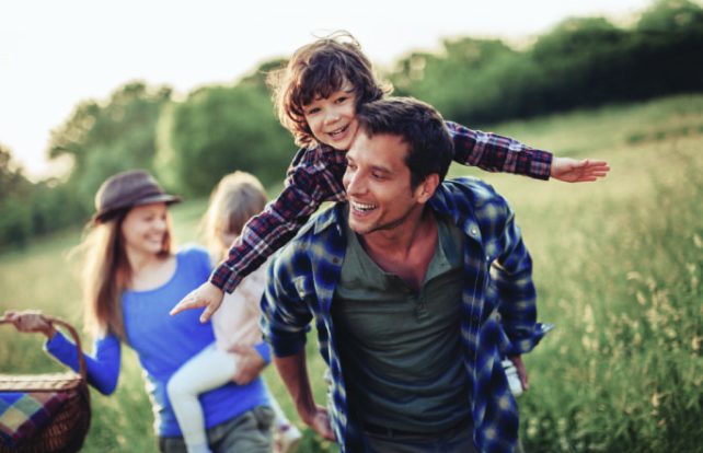 father with son on his shoulders in a field, mother holding daughter in background