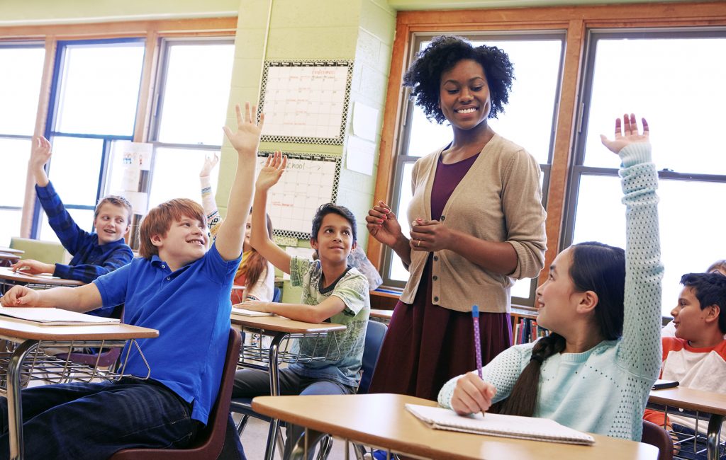 School, tutor and students raise their hands to ask or answer an academic question for learning. Diversity, education and primary school kids speaking to their woman teacher in the classroom